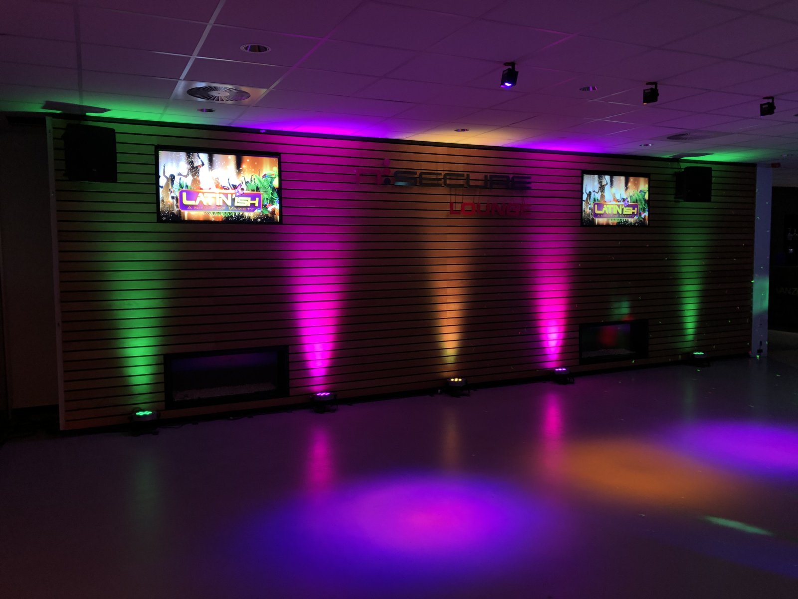 Zaal met gekleurde uplights, schermen en dansvloer bij Latin'ish