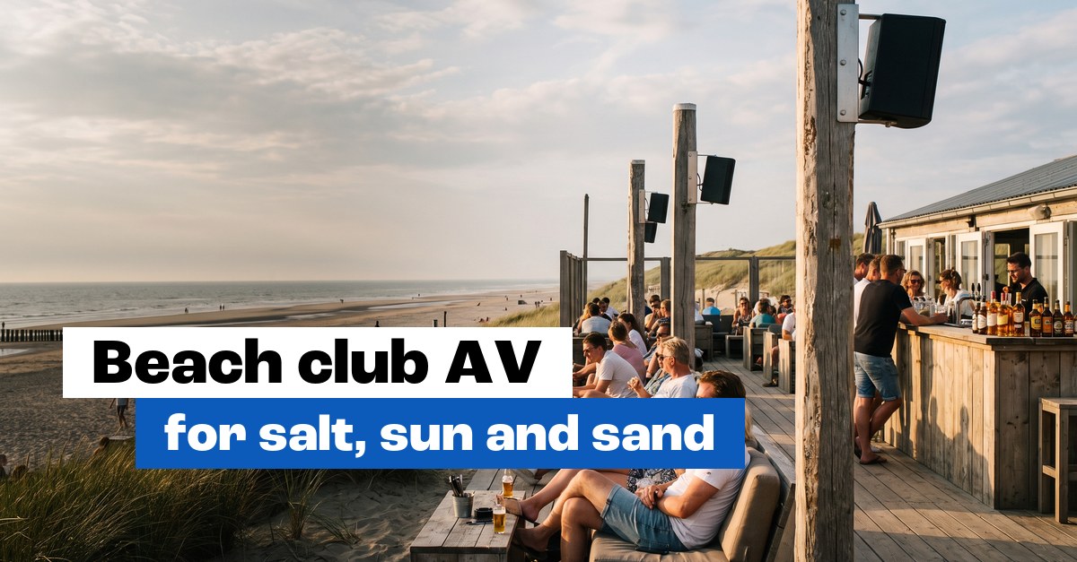 Beach club terrace by the sea with speakers on wooden posts and guests at the bar