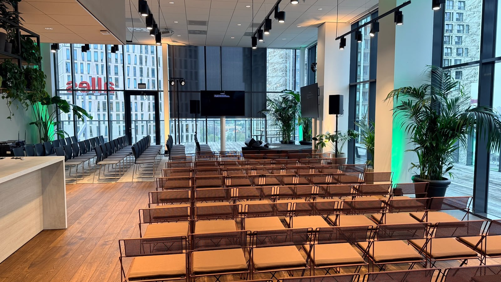 Lege zaal in BLAAK16 op woensdag: stoelen in rijen, podium, speakers, twee schermen en groen licht staan klaar